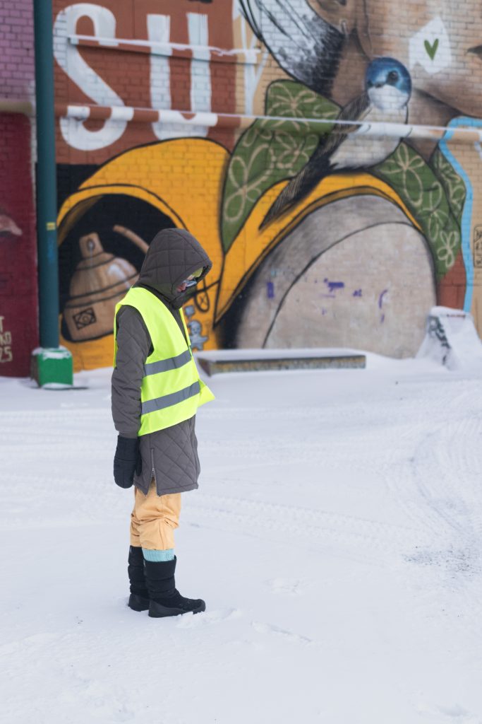 Hanna seisoo sivuttain ulkona seinän ja lintumuraalin edessä katse alas päin